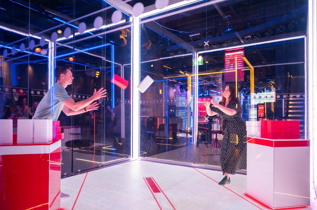Two people in The Cube simulation throwing a foam brick to each other in a game 